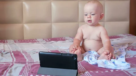 Cute kid sitting on the bed and stares cartoons on the tablet PC. Tiny one-year Stock Footage