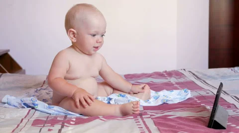 Cute kid sitting on the bed and stares cartoons on the tablet PC. Tiny one-year Stock Footage