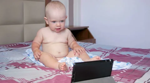 Cute kid sitting on the bed and stares cartoons on the tablet PC. Tiny one-year Stock Footage 67722507