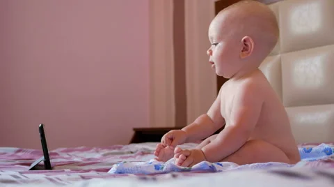 Cute kid sitting on the bed and stares cartoons on the tablet PC. Tiny one-year Stock Footage 67722926
