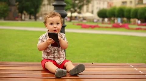 Cute kid is sitting on a bench with smartphone  Stock Footage 65435158