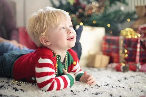 Cute kid sitting on the carpet, in front of the christmas tree Stock Photos