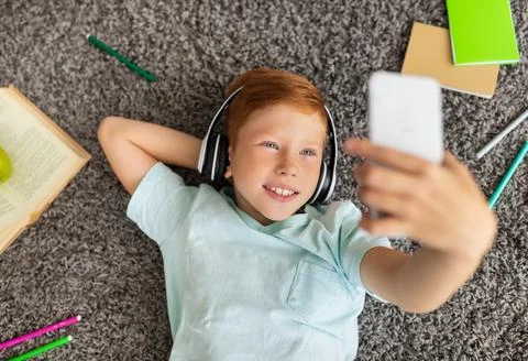 Cute kid using headset and cellphone while doing homework Stock Photos