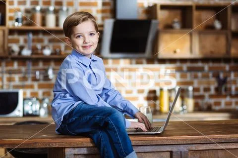 Cute kid using laptop in the kitchen Stock Photos