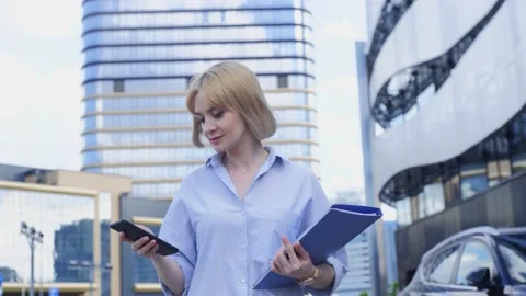 A cute lady with papers looking at her smartphone going to the business meeting Stock Footage 168919746