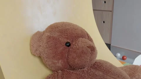 Cute large fluffy brown teddy bear resting on a yellow surface in a playroom. 動画素材 344089866