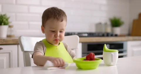 Cute little baby boy eats strawberries from green plate and wipes table with rag Stock Footage 154558041