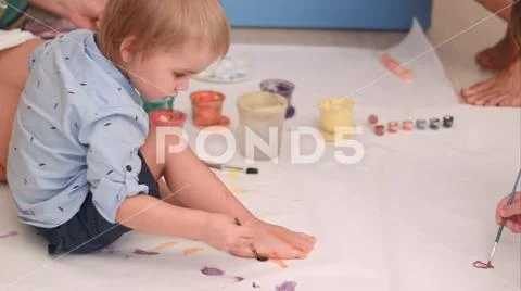 Cute little baby boy painting his feet on a large blank white paper Stock Photos