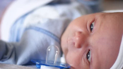 A cute little baby is looking into the camera and is happy on a white bed sheet Stockbeeldmateriaal 73560672