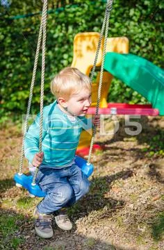 Cute little blond boy swinging on swings outdoor playground Stock Photos