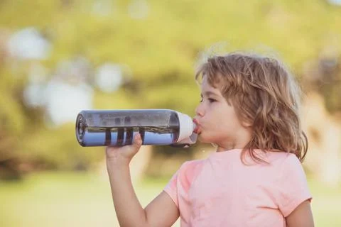 Cute little boy drink water from sport bottle in green park. Closeup portrait of Stock Photos