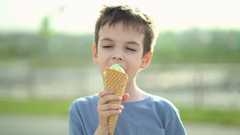 Cute little boy eats green ice cream cone outdoors making funny playful face Vídeo Stock 337006294