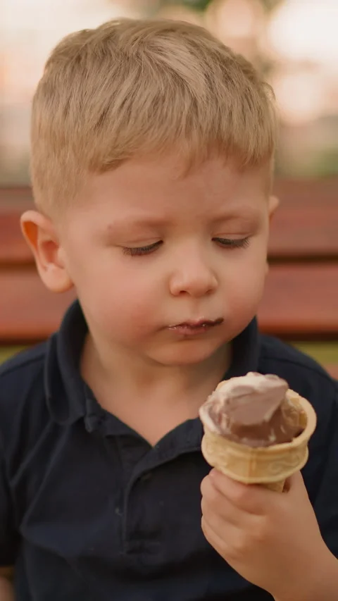 Cute little boy eats ice cream in wafer cone on bench Stock Footage 307774087