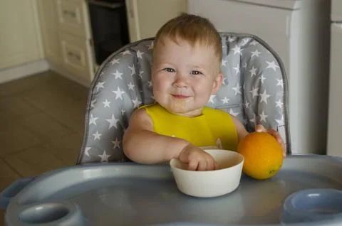 Cute little boy eats an orange at a children's table. Stock Photos