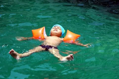 Cute little boy is floating on back in the swimming pool, wearing swimming cap a Stock Photos