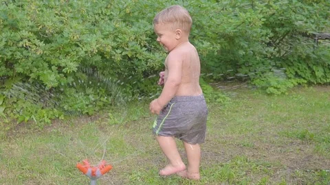 Cute little boy having fun outside with water sprinkler in summer garden. Slow Video stock 90496324