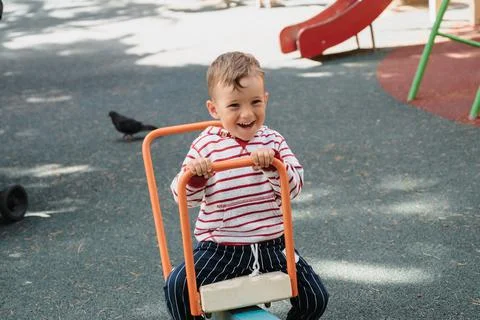 A cute little boy is having fun on the playground, riding on a swing. Stock Photos