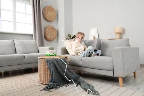 Cute little boy with laptop using nebulizer on sofa at home Stock Photos