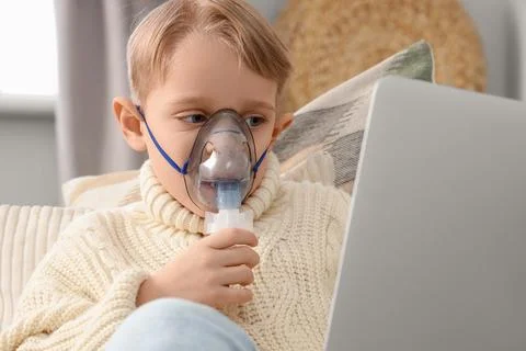 Cute little boy with laptop using nebulizer at home, closeup Stock Photos