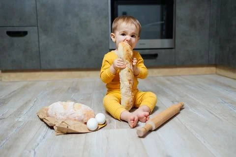 A cute little boy one year old sits and eats freshly baked rye bread. The c.. Stock-Fotos