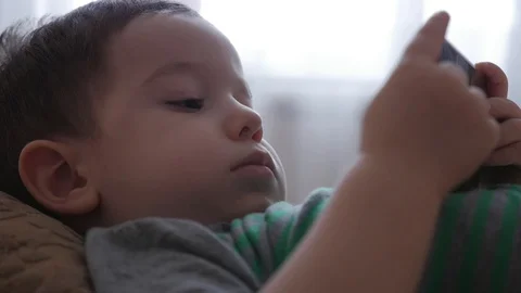 Cute little boy playing on the phone, lying on his sofa, playing with the tablet Stock Footage 101487567