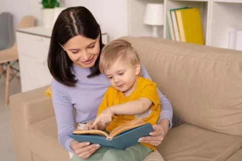 Cute little boy pointing at picture on page of book while discussing fairy tale Stock Photos