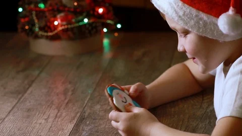 Cute little boy in a red hat examines Christmas gingerbread cookies Stock Footage 113599005