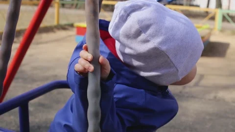 A cute little boy sits on a swing in the spring in a cap Stock Footage 152312364