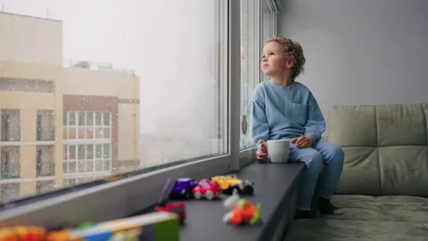 Cute little boy is sitting alone in children room with many of toys, cozy home Stock Footage 181865713