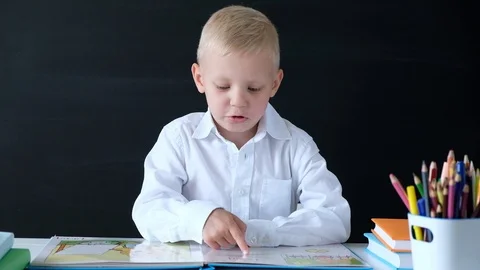 Cute little boy sitting at the table and reading. Child from elementary school Stock Footage 111759638