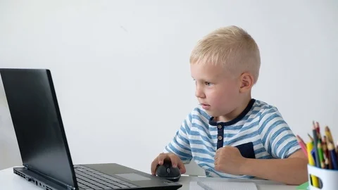 Cute little boy sitting at the table and playing or working on a computer. Child 動画素材 111759702