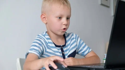Cute little boy sitting at the table and playing or working on a computer. Child 스톡 동영상 111759846