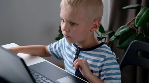 Cute little boy sitting at the table and playing or working on a computer. Child Stock Footage 111760052
