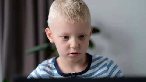 Cute little boy sitting at the table and playing or working on a computer. Child 스톡 동영상 111760152
