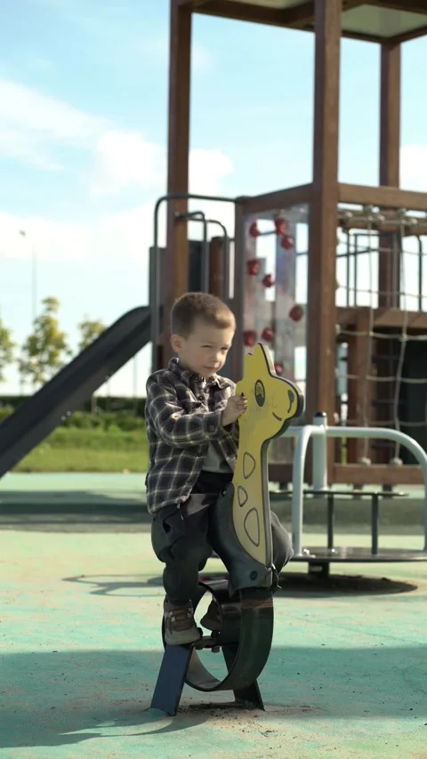Cute little boy smiling while rocking on a yellow giraffe spring toy at a Vídeo Stock 345528844