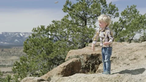 Cute little boy throws rock off mountain top cliff, dangerous risk to hikers Stock Footage 248580045