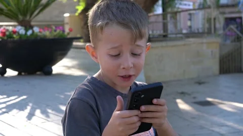 Cute little boy using smartphone outdoors with surprised expression 스톡 동영상 341328017