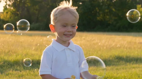 Cute little boy in white polo-shirt playing outdoors, blowing soap bubbles 库存影片 112526020