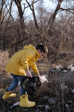 A cute little boy in yellow jacket and rubber boots is collecting garbage out Stock Photos