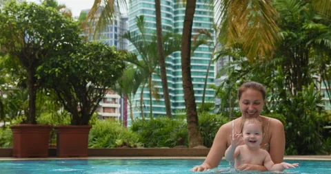 Cute little child bathing with her mom in blue street pool in courtyard Stock Footage 231859799