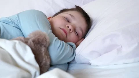 Cute little child boy sleeping in cozy white bed lying on pillow with teddy b Stock Footage 135466498