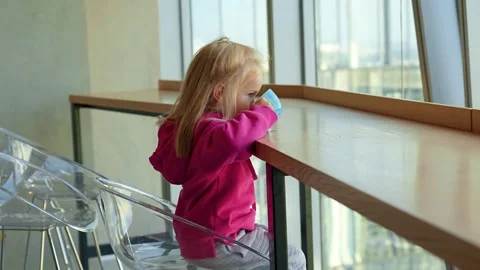 Cute little child sits at a table and drinks from a mug in front of panoram.. Stock Footage 319639666