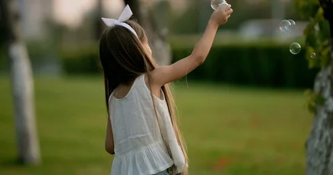 Cute little girl is blowing soap bubbles in the garden outdoors on a sunny day Stock Footage