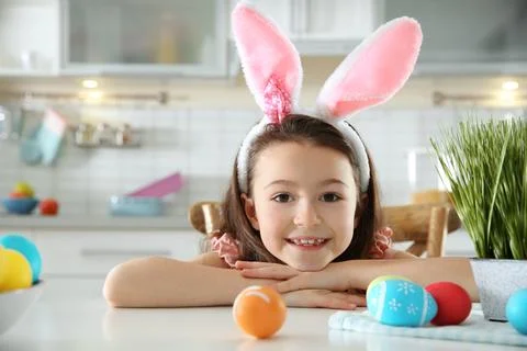 Cute little girl with bunny ears headband and painted Easter eggs sitting at  Stock Photos