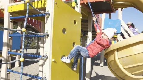 Cute little girl is climbing up on ladder in playground equipment Stock Footage