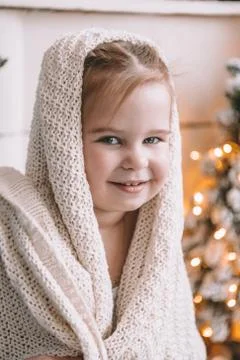 Cute little girl covered in a big plaid or scarf at home Stock Photos