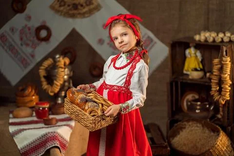 Cute little girl in folk costume holds basket of bagels in traditional house Stock Photos