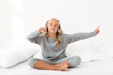 Cute little girl in gray pajamas listening to music with closed eyes while si Stock Photos
