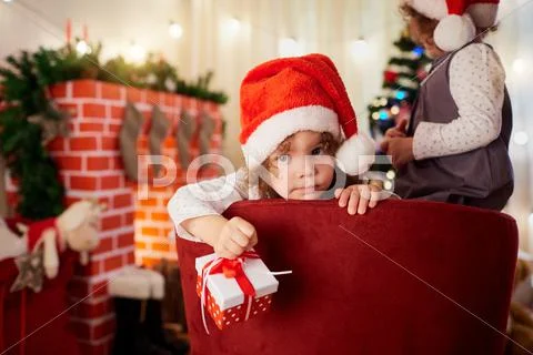 Cute little girl in the hat of Santa Claus with a gift in hand looking at the Stock Photos