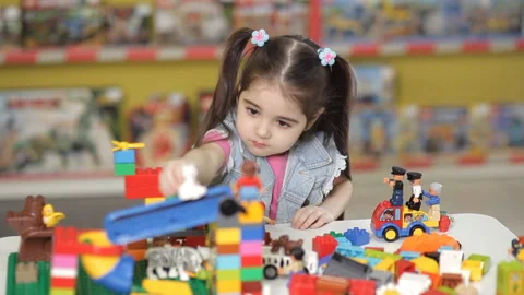 Cute little girl is playing with objects made of plastic elements, blocks of Stock Footage 87960138